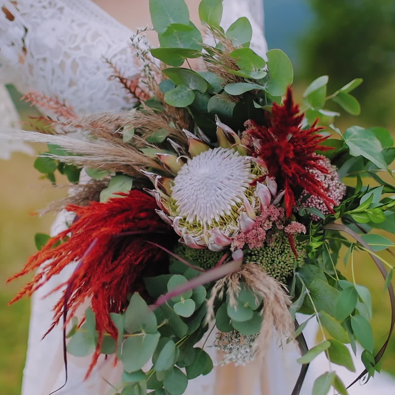 Bouquet of exotic flowers in woman's hands. Bride in wedding white dress holding wild flowers among nature in summer. Close-up.
