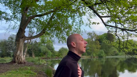 young bald man breathwork near lake