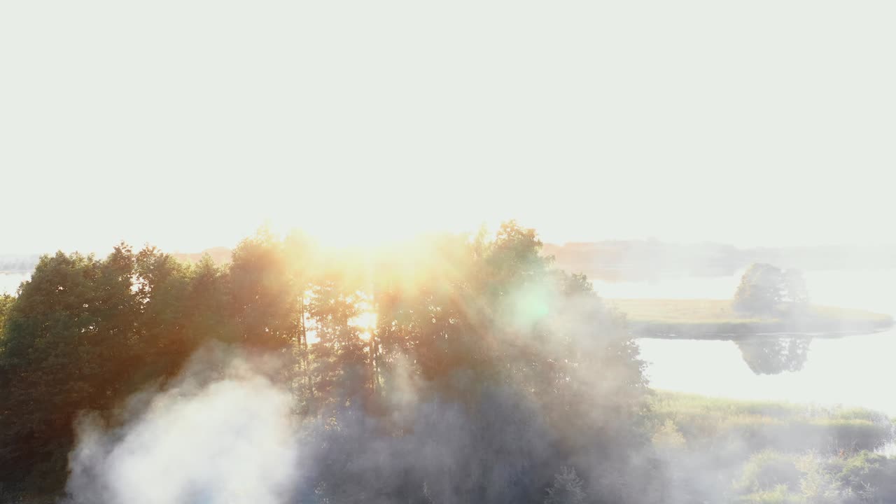 여름의 놀라운 해가 뜨는 호수 연안에서 캠프 불에서 연기가 아오르고, 아름다운 렌즈 플레어 자연 배경 풍경.