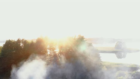 smoke rising from campfire over amazing summer sunrise lake shore, beautiful lens flare nature background scenery.