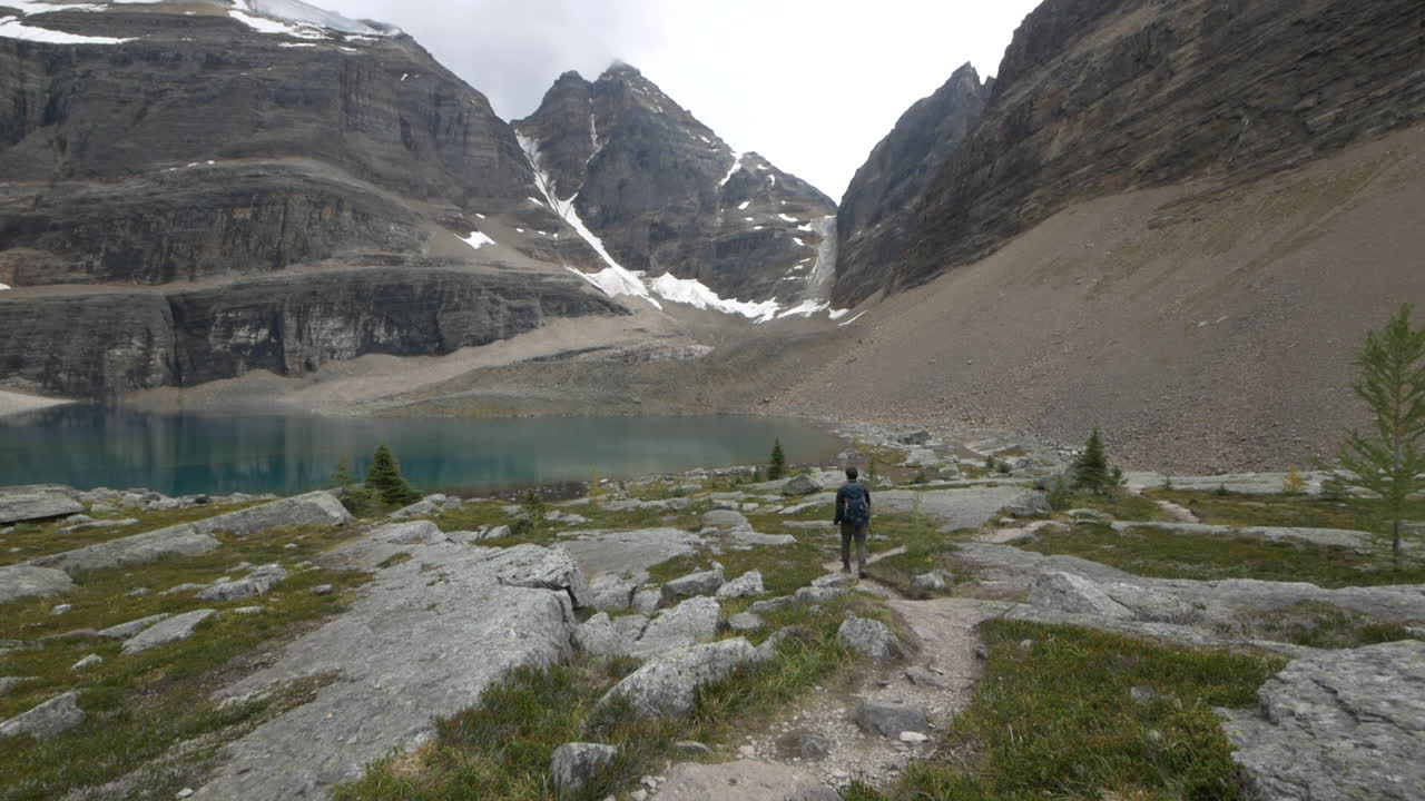A young couple navigating through rocks and scrub on the turquoise shore of Lake O'Hara, Alberta, Canada.