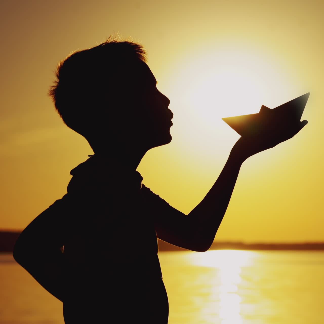 Paper boat is in the hands of a child. Beautiful summer sunset. Origami
