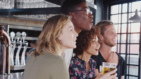 group of male and female friends celebrating whilst watching game on screen in sports bar