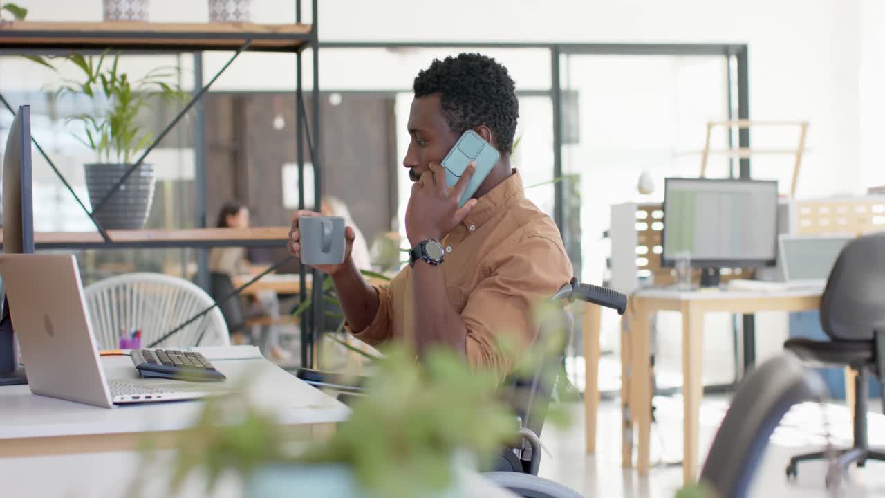 Handicappet afroamerikansk forretningsmand i kørestol med kaffe taler i smartphone i slowmotion