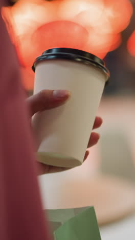 primer plano de una dama con un vestido rosa sosteniendo una taza de café mientras camina por un restaurante, el fondo presenta sillas borrosas, mesas y luces rojas brillantes que también se reflejan en el suelo