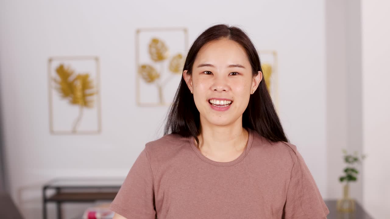 Asian woman covers ears in discomfort, reacting to noise in bright, modern living room