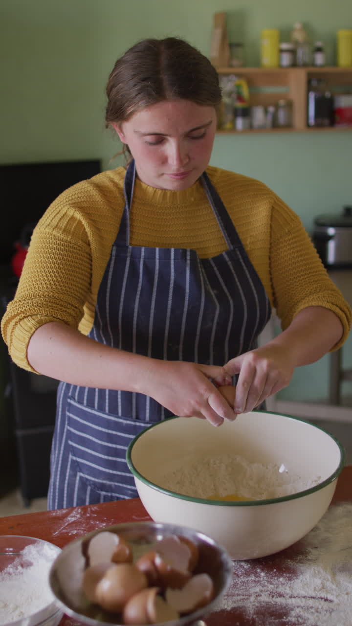 video vertical de una mujer caucásica horneando, rompiendo huevos en un cuenco de mezcla en una cocina de campo