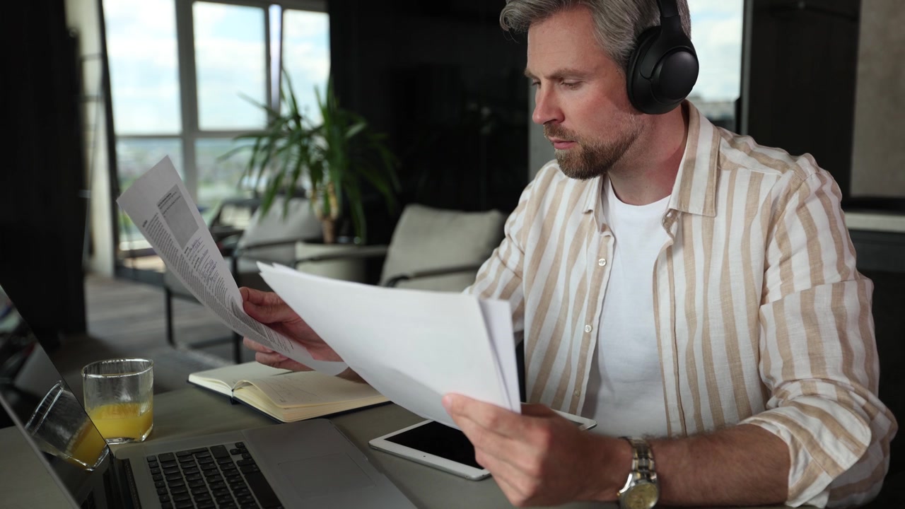 Focused Man in Headphones Reading Documents at Home Office Desk
