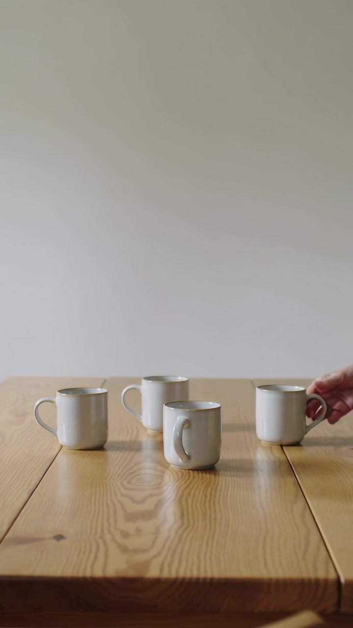 Vertical video: Entering woman placing 4 white mugs on wood table at home for coffee in sweater
