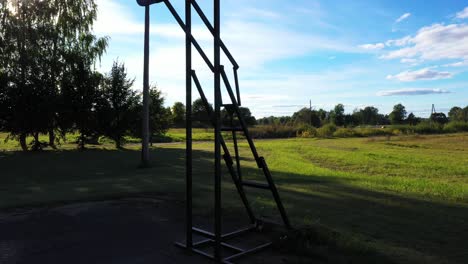 Old-basketball-board-and-hoop-in-rural-landscape-on-sunny-day,-close-up-ascend-view