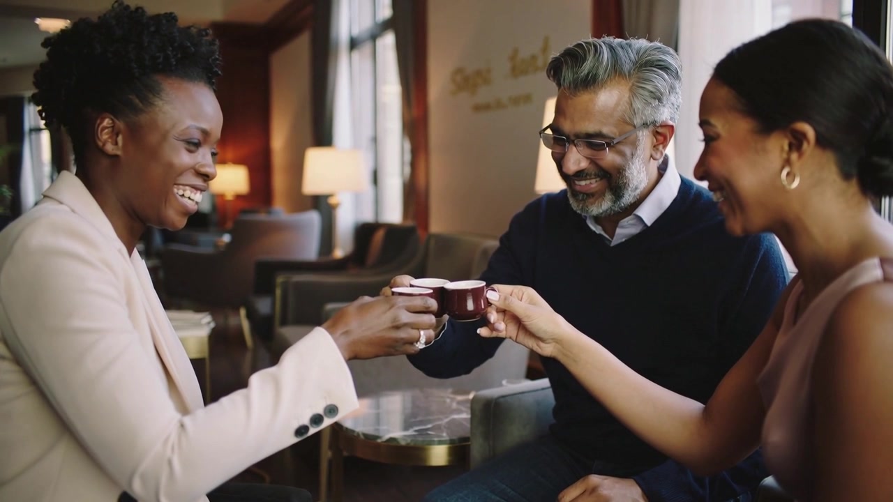Trois collègues en tenue d'affaires, levant leurs tasses à expresso et trinquant à une table de café chaleureuse, célébrant