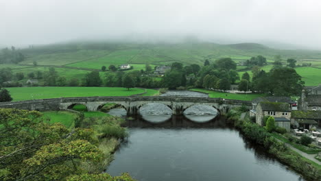 Slowly-tracking-forwards-over-trees-towards-bridge-in-overcast,-Yorkshire,-United-Kingdom