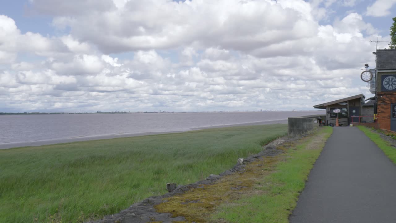 Seafront path in Hessle leading to a brick pub, cloudy sky and picnic benches outside