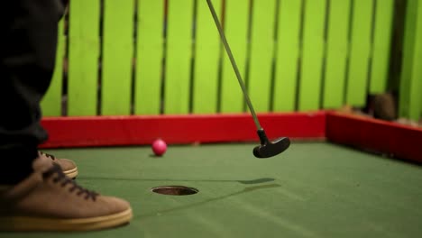 un jugador pone una pelota rosa en un campo de mini-golf, logrando un rebote y un hoyo en uno.