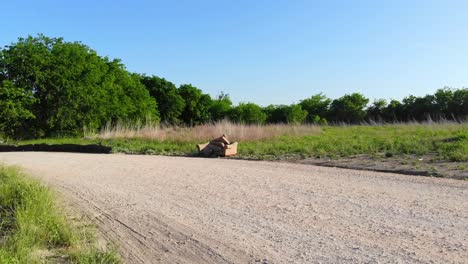 Flying-directly-over-a-mountain-bike-laying-on-its-side-and-across-a-gravel-road,-towards-an-abandoned-tan-couch-that-was-ditched-on-the-wide-of-the-road