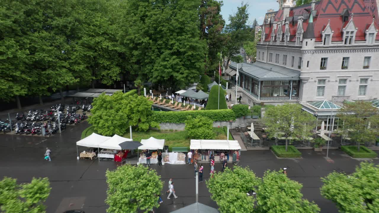 Drone pulling back from buffet at outdoor cafe and revealing Hotel Chateau d'Ouchy and the Lausanne city skyline in Switzerland