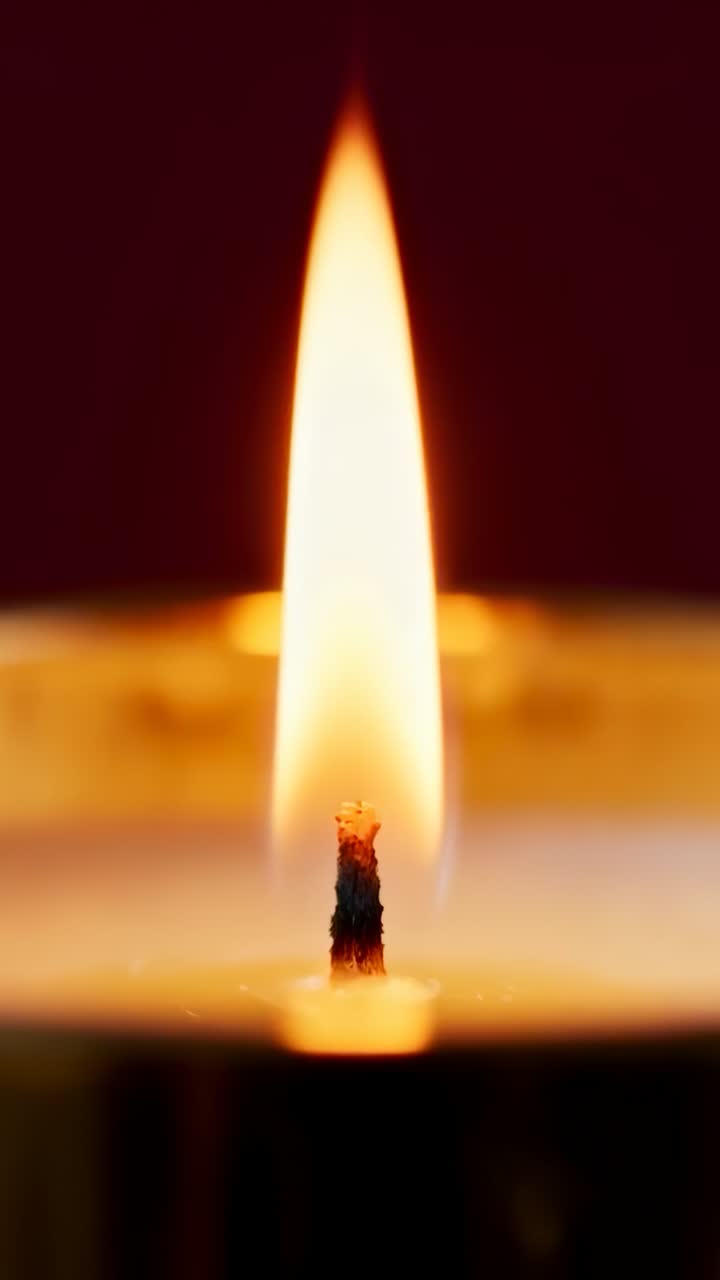 Video verticale: fiamma di lumino da tè che danza, inizialmente stabile, tremolante e inclinata in una stanza poco illuminata