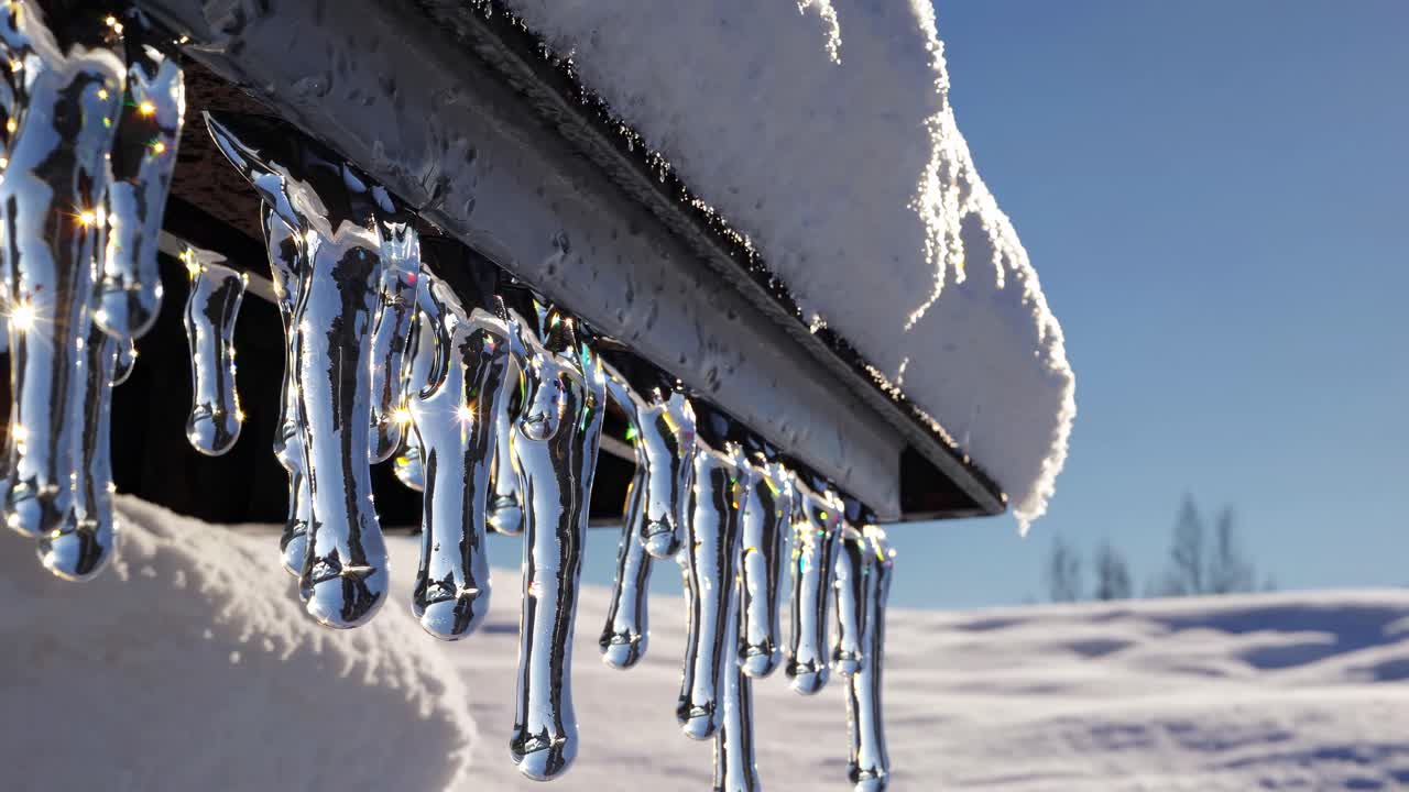 Close-up, low-angle shot of icicles hanging from a snow-covered roof, glistening in sunlight