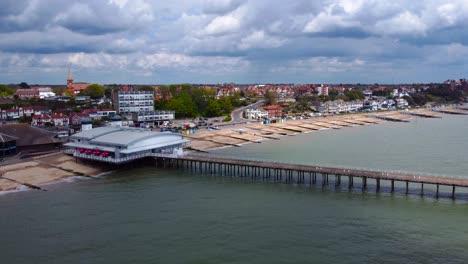 Seagull-flying-in-front-of-a-drone-capturing-an-aerial-footage-of-a-beachfront-and-harbor,-revealing-houses-and-buildings-plus-the-gorgeous-clouds-and-sky