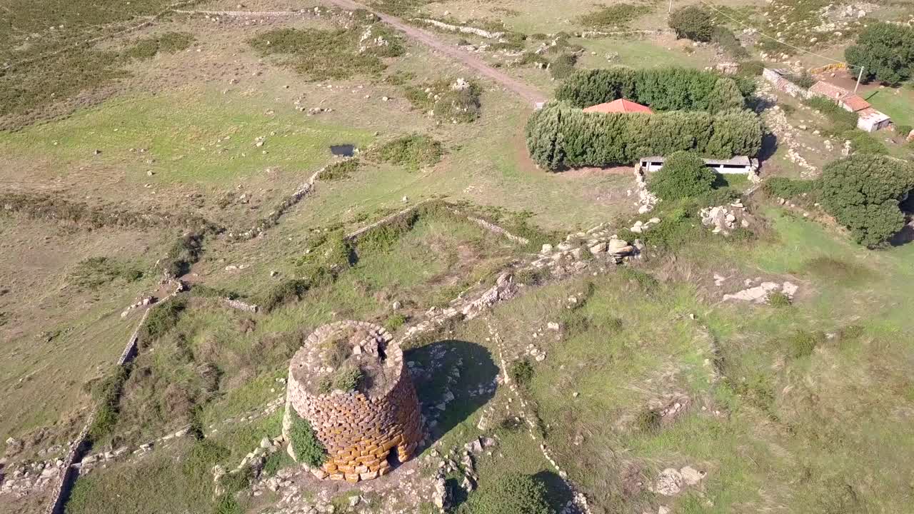 Sardinia, Drone Aerial shot backwards discovering a Nuraghe a monolith prehistorical construction in the island of Sardinia in Italy. the drone is flying towards the tower and then tilting over it.