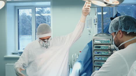 doctor adjusts lamp in surgery room. focused surgeon with binoculars wearing uniform prepares to conduct coronary artery bypass surgery in clinic