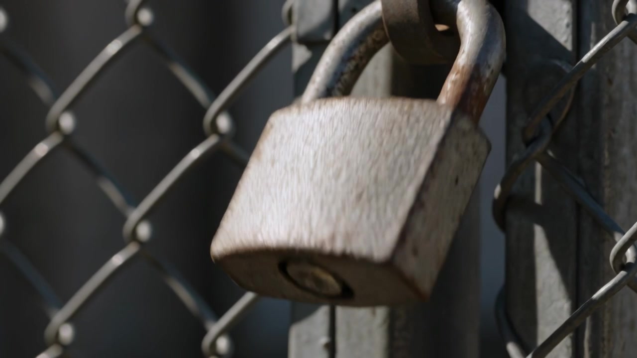 Panning camera capturing rusty padlock swinging at outdoor gate, revealing pitted keyhole