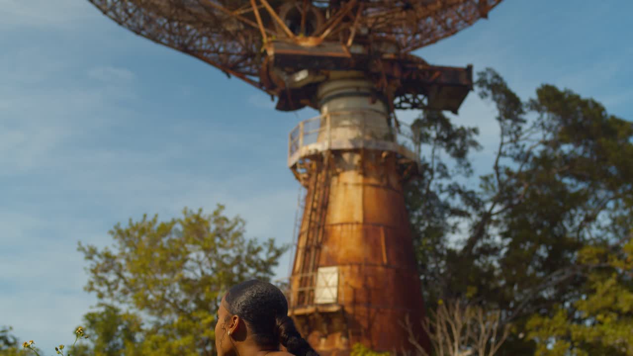 vista asombrosa mientras una joven huele las rosas antes de mirar hacia una enorme estación de seguimiento de torres de radar