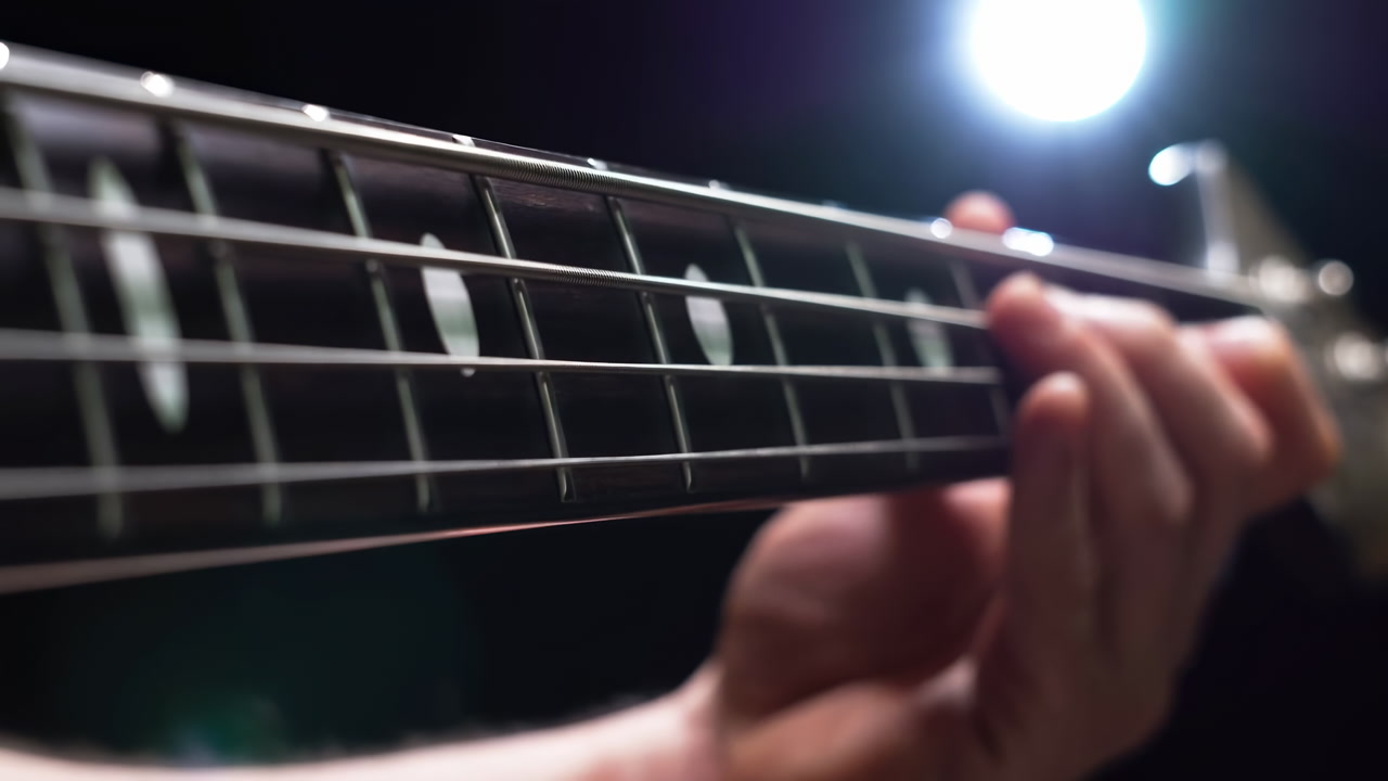 Closeup Hand On Bass Fretboard, Session Bassist Practicing Fingerstyle Lines Under Studio Spotlight Focusing