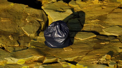 black trash bag lay on a rocky beach