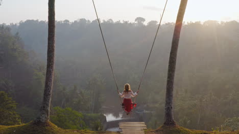 aerial view woman swinging over tropical rainforest at sunrise sitting on swing with view of river enjoying having fun on holiday travel freedom