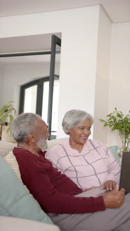 vertical video of happy senior biracial couple using laptop, unaltered, in slow motion