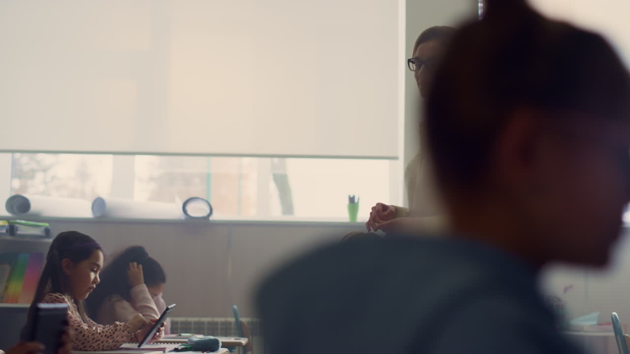 el maestro camina entre los escritorios. los alumnos buscan en internet en tabletas digitales