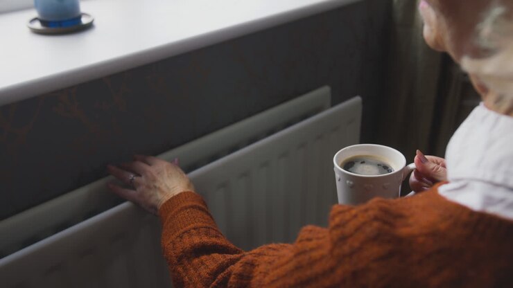 Senior Woman In Wheelchair Trying To Keep Warm By Radiator During Cost Of Living Energy Crisis