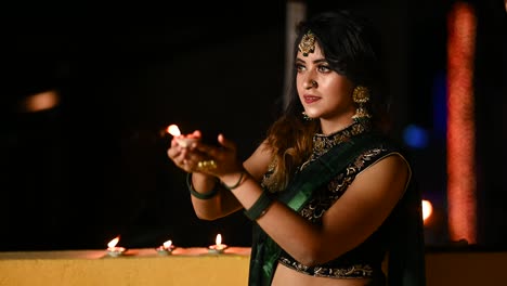 beautiful young woman lighting diya - oil lamp in traditional clothing on the occasion of diwali.