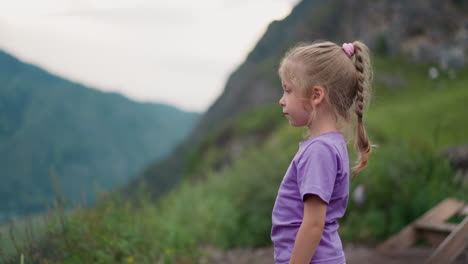 calm litle child stands on hill looking at distant mountains