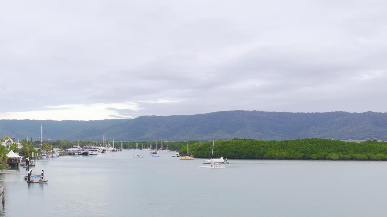 A serene view of a marina with boats and lush greenery under overcast skies in Port Douglas, Australia