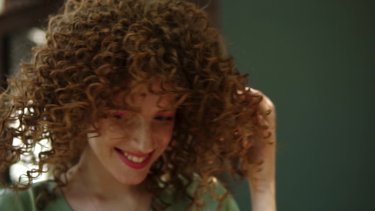 전문적인 분홍색 메이크업을 한 예쁜 홍색 소녀의 초상화 미소. 그녀는 재미를 느끼고 있습니다. 녹색 블라우스를 입고, 머리를 돌리고 카메라에 기 ⁇ 게 웃고, 그녀의 완벽한 헤어 스타일을 만지고 있습니다. 야외. 느린 동작