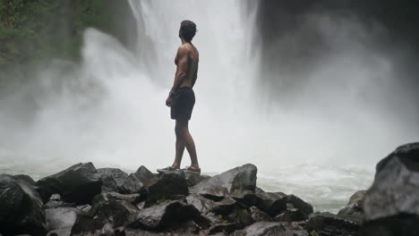 rising shot of man standing in front of powerful la fortuna jungle waterfall