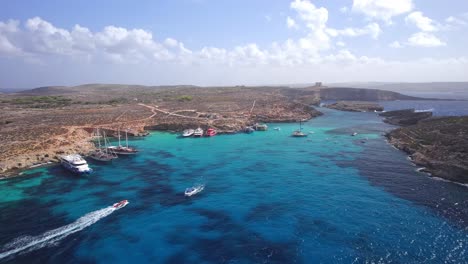 fast drone descends into blue lagoon following tourist speed boat, comino island, malta