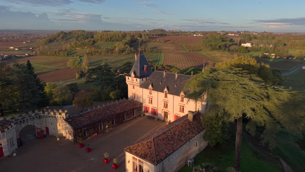 Bright sunlight breaks over a stunning castle of Pressac, illuminating lush gardens and towering trees. The peaceful morning creates a serene atmosphere perfect for exploration