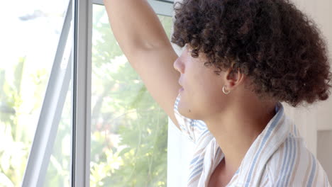 young man looking out window, enjoying sunny day with relaxed expression, at home