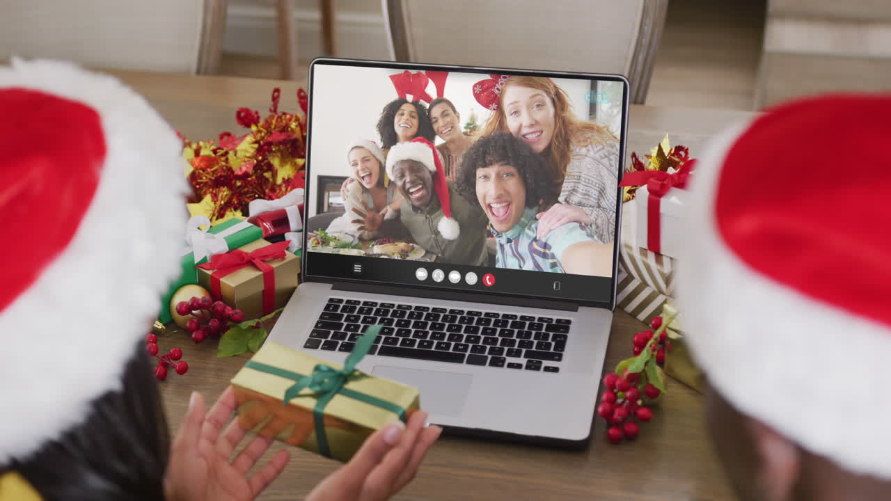 animación de una pareja diversa con sombreros de papá noel en una llamada de video portátil con amigos en navidad