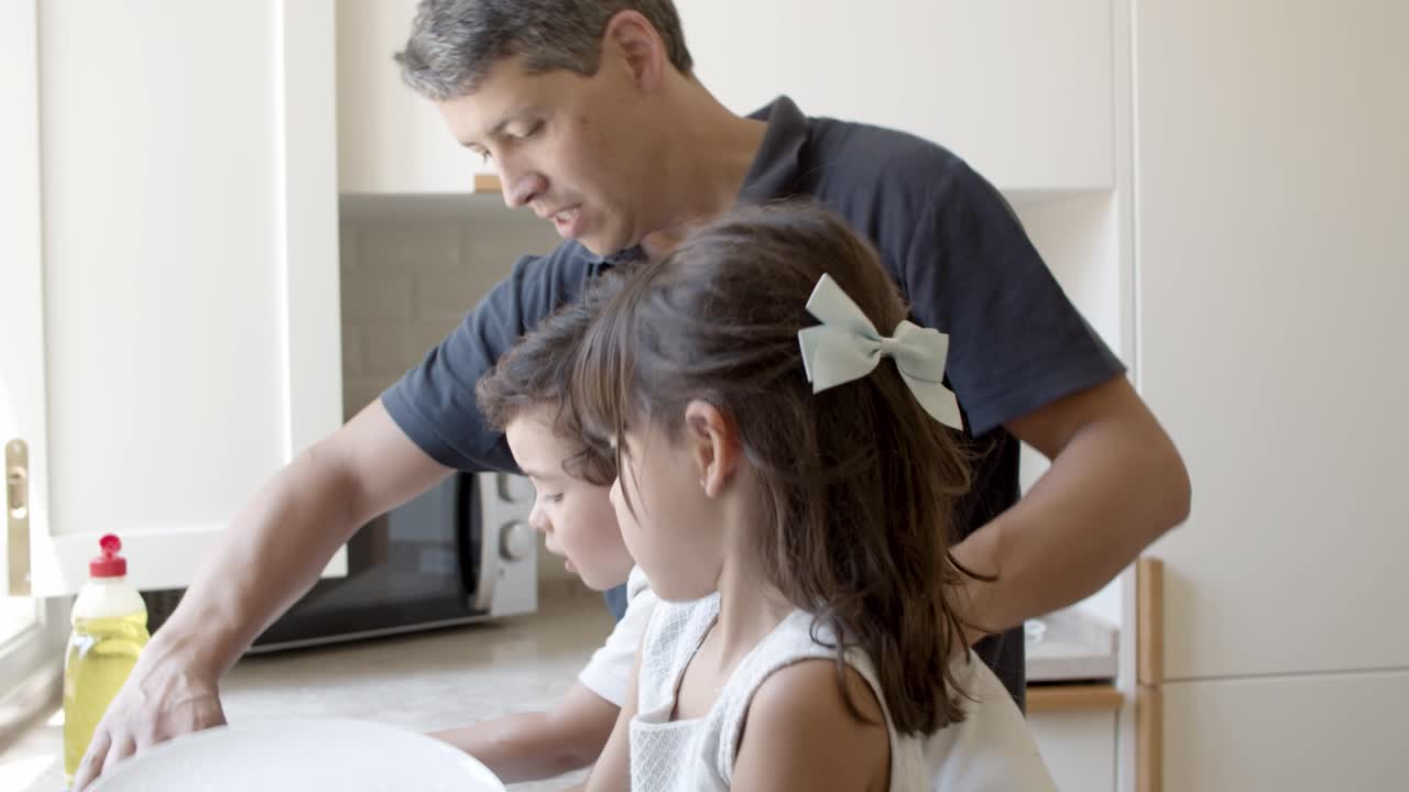 papá y el hermano pequeño ayudando a la niña a lavar los platos