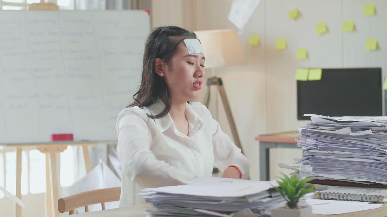 병든 아시아 여성은 사무실에서 문서와 함께 열심히 일하면서 종이를 버립니다.