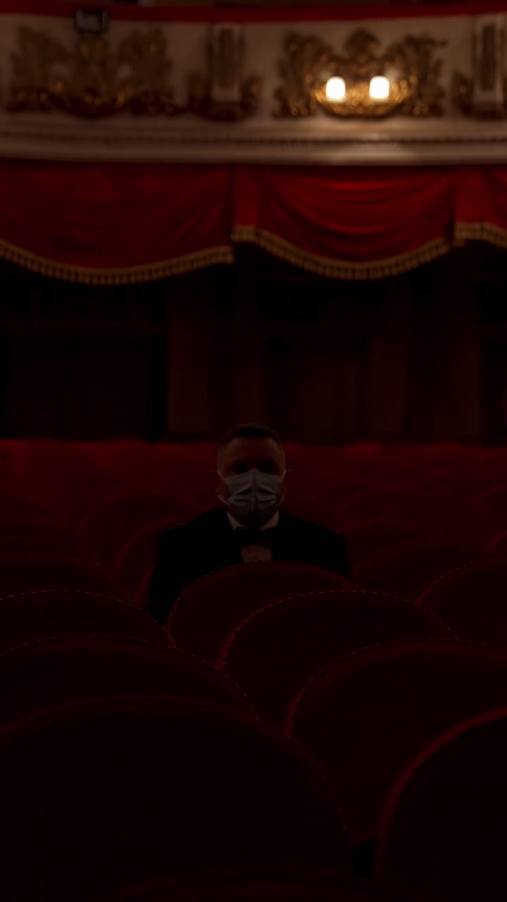 Man stands up from a red theater chair and throws medical mask away. Visitor in empty hall. Stop pandemic concept. Vertical video
