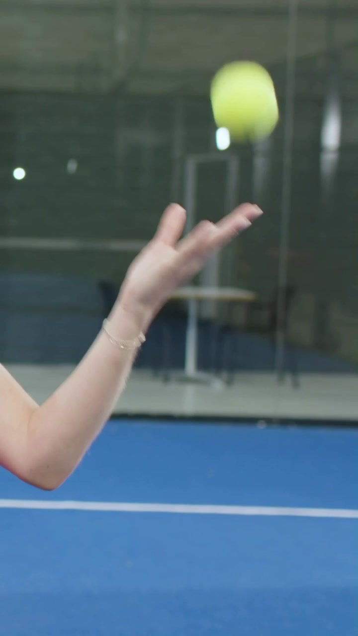 Vertical video: Raising arm, woman in pink tossing ball on blue court, practicing serve, copy space