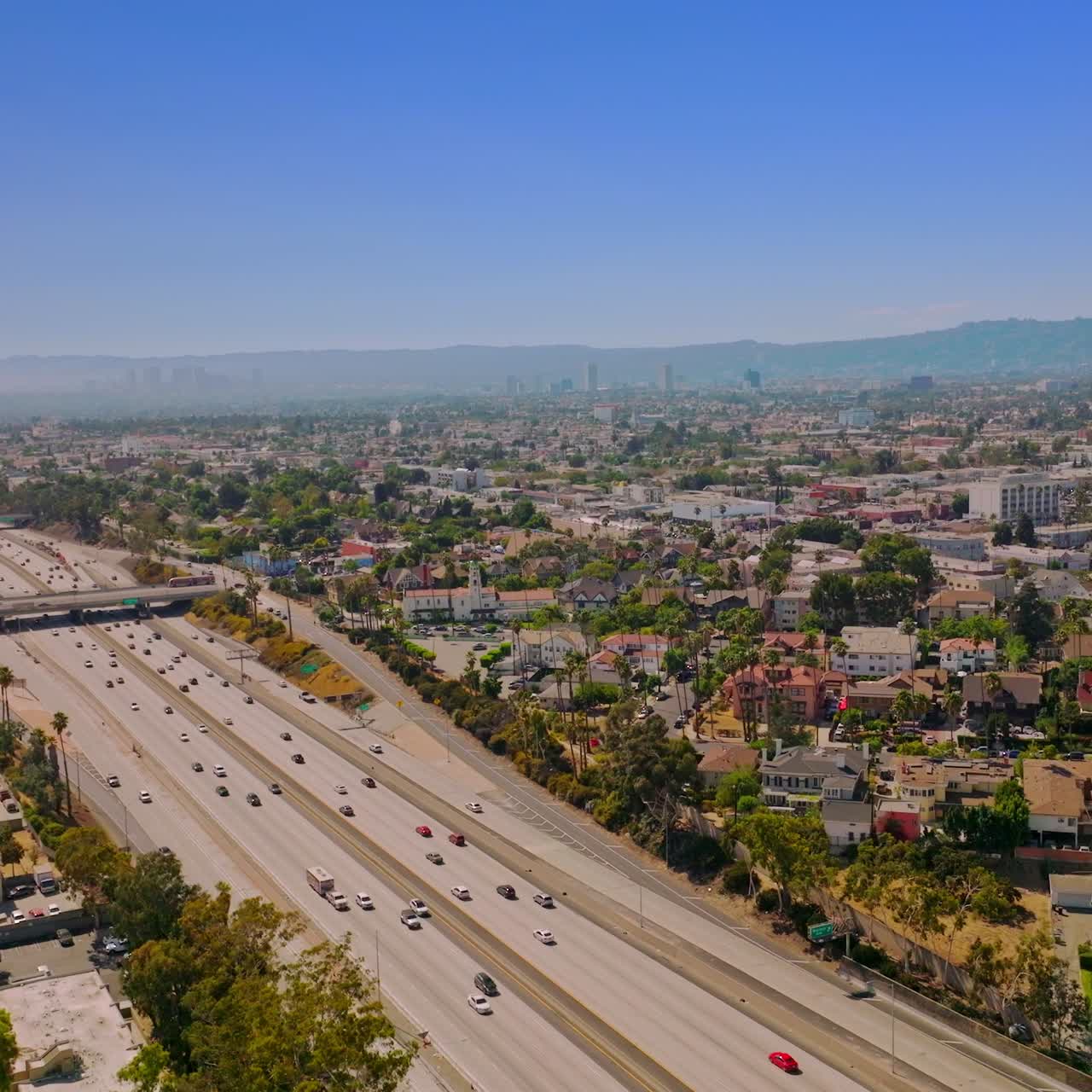 Quickly moving cars by the multi-lane freeways of Los Angeles, California, USA. Amazing clear blue sky at backdrop. Rising drone footage