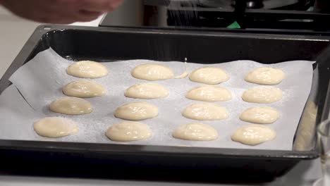 a person prepares macaron batter by piping small discs onto parchment paper. the process takes place in a contemporary kitchen with a clean, organized workspace