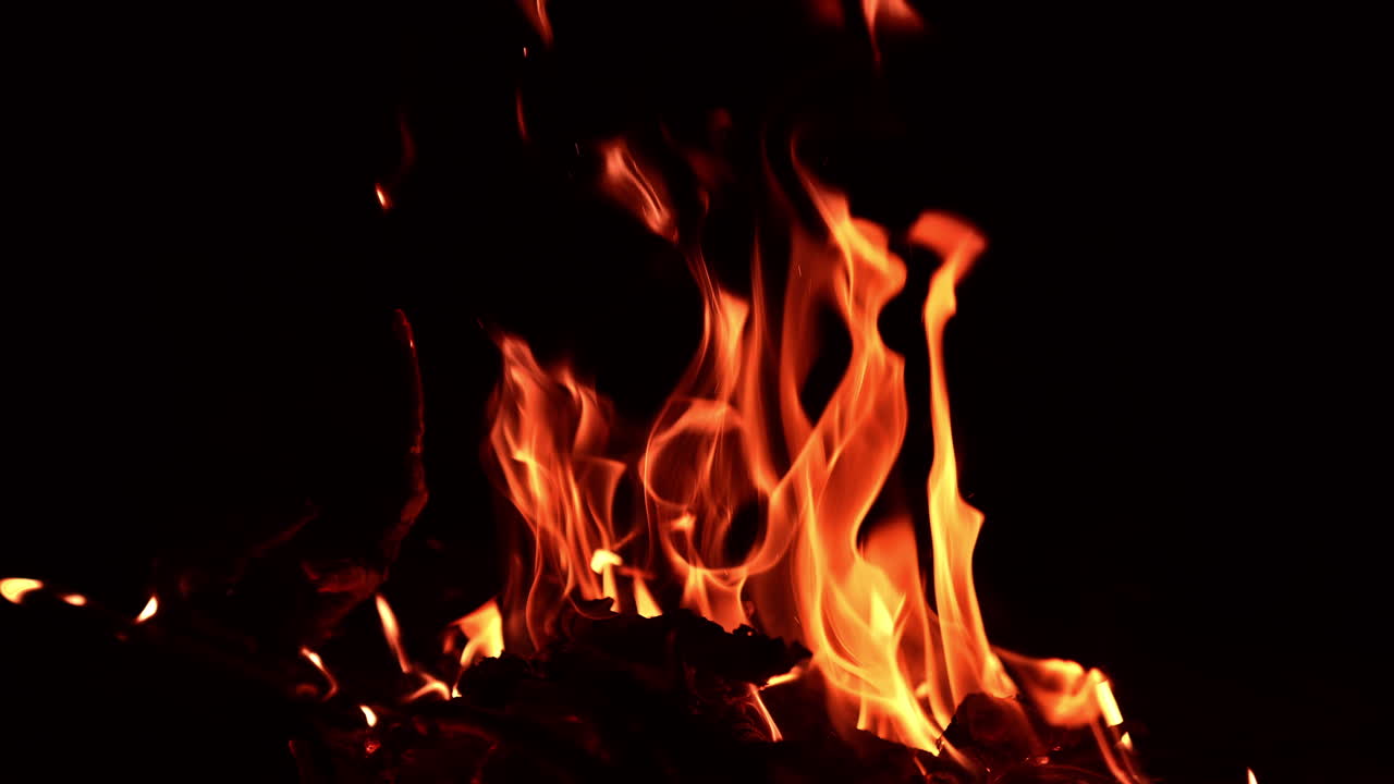 Wooden logs burning in the campfire at night. One sticks breaks and multiple sparkles rise up.