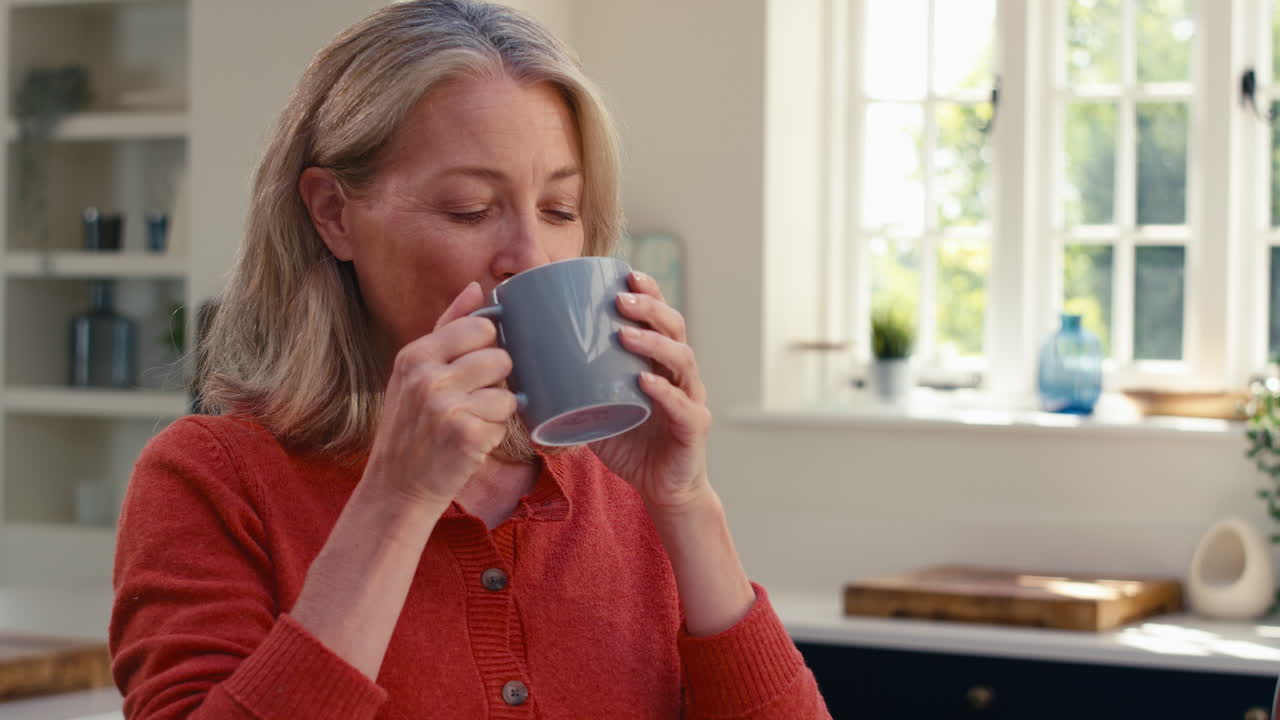 Close Up Of Smiling Mature Woman Standing In Kitchen Relaxing With Cup Of Coffee